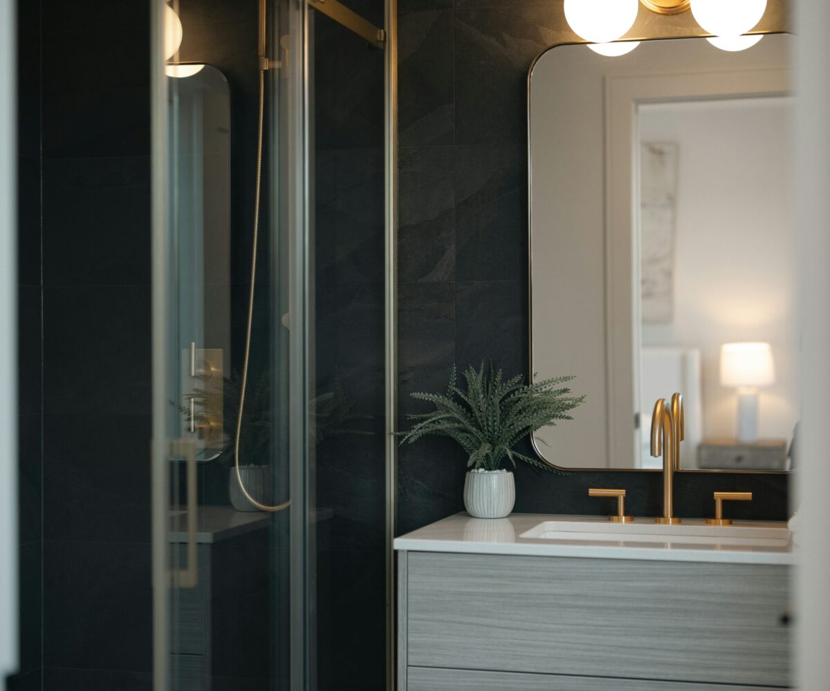 Dark tiled bathroom with pale wood vanity and warm brass fixtures