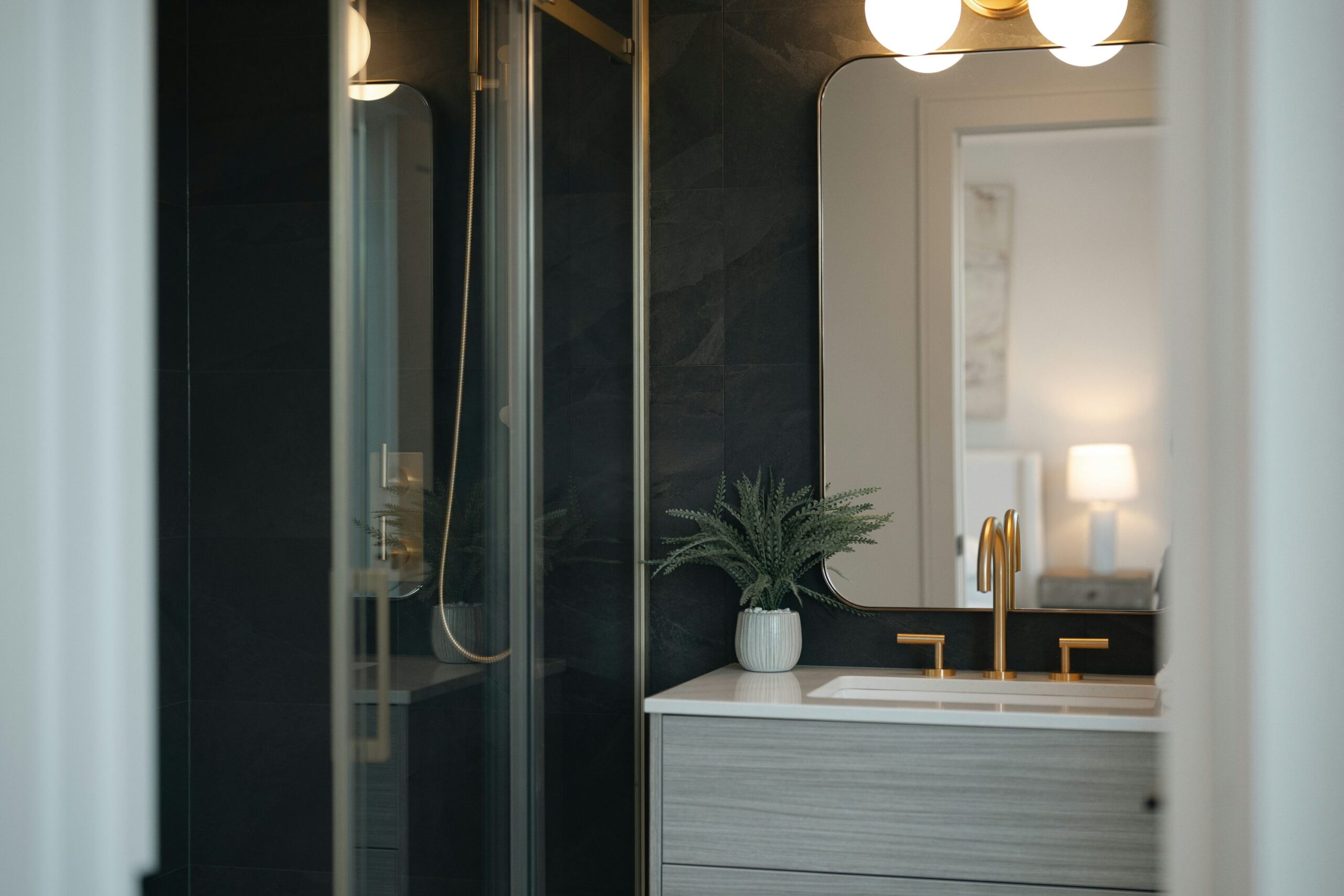 Dark tiled bathroom with pale wood vanity and warm brass fixtures
