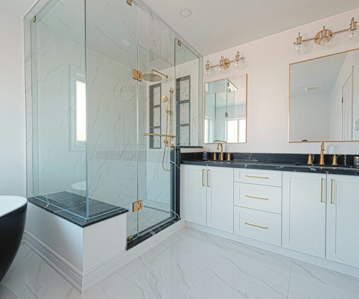 White ensuite with black stone counter, brass fixtures and glass shower