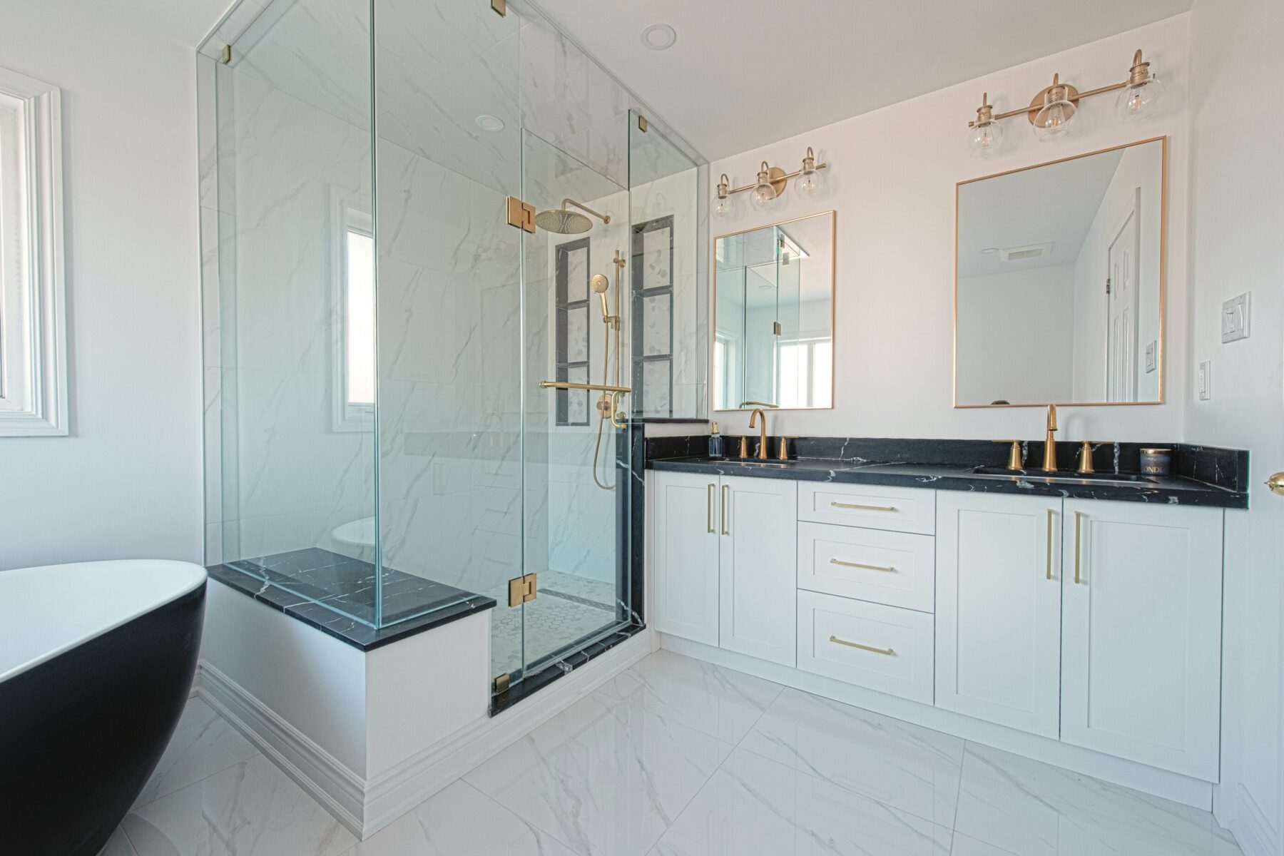 White ensuite with black stone counter, brass fixtures and glass shower