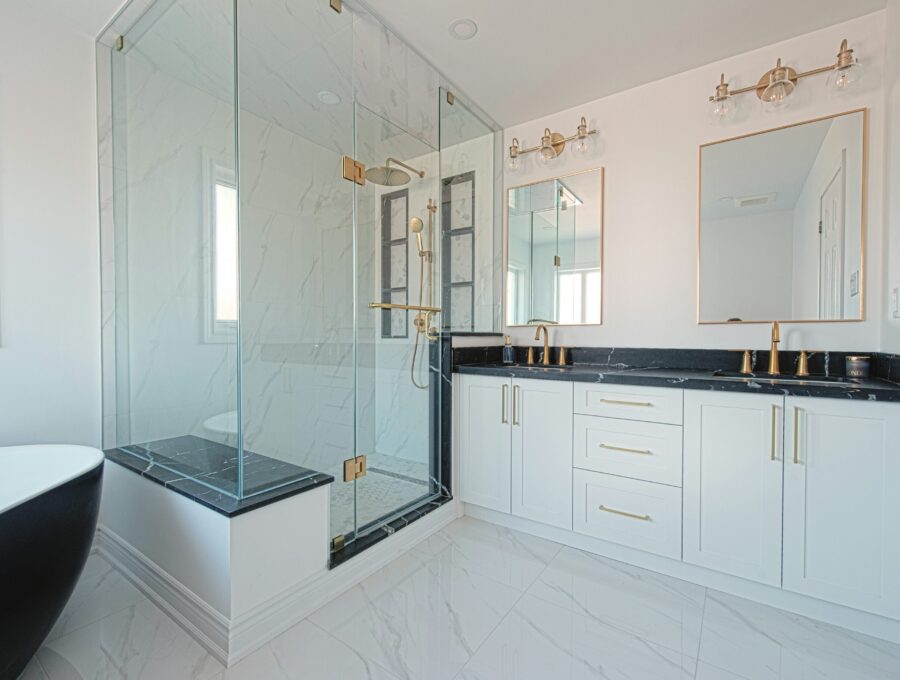 White ensuite with black stone counter, brass fixtures and glass shower